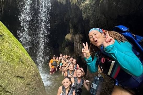 Grupo sonriente dentro de una cueva de roca con una cascada al fondo
