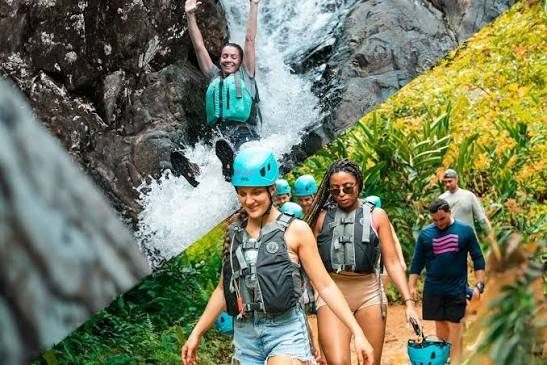 Grupo con casco y chaleco salvavidas junto a una cascada y caminando entre la vegetación del cañón