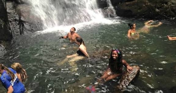 Bañistas en una poza al pie de una cascada ancha que cae sobre la roca